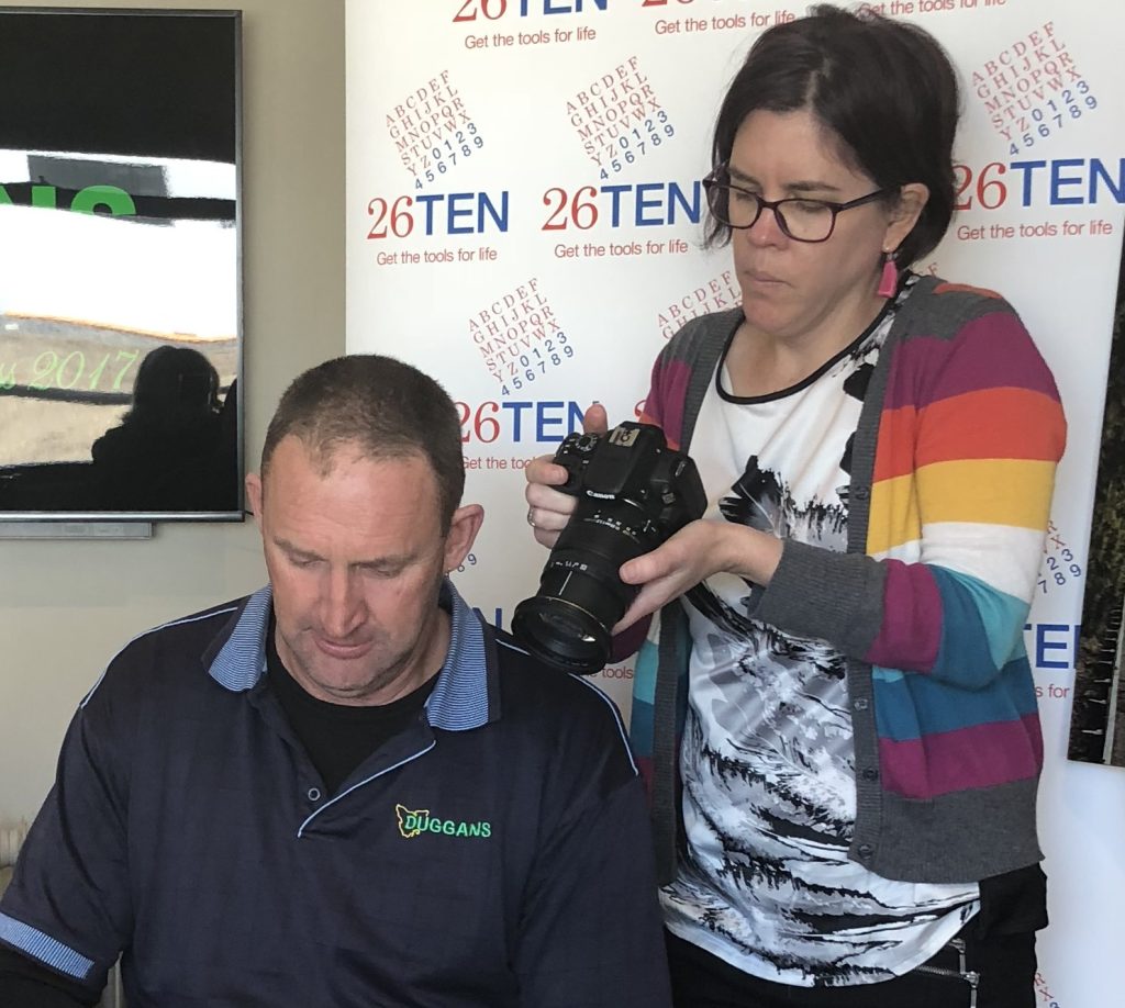 Photo Nicole Alley holding a camera and standing behind Rodney Duggan