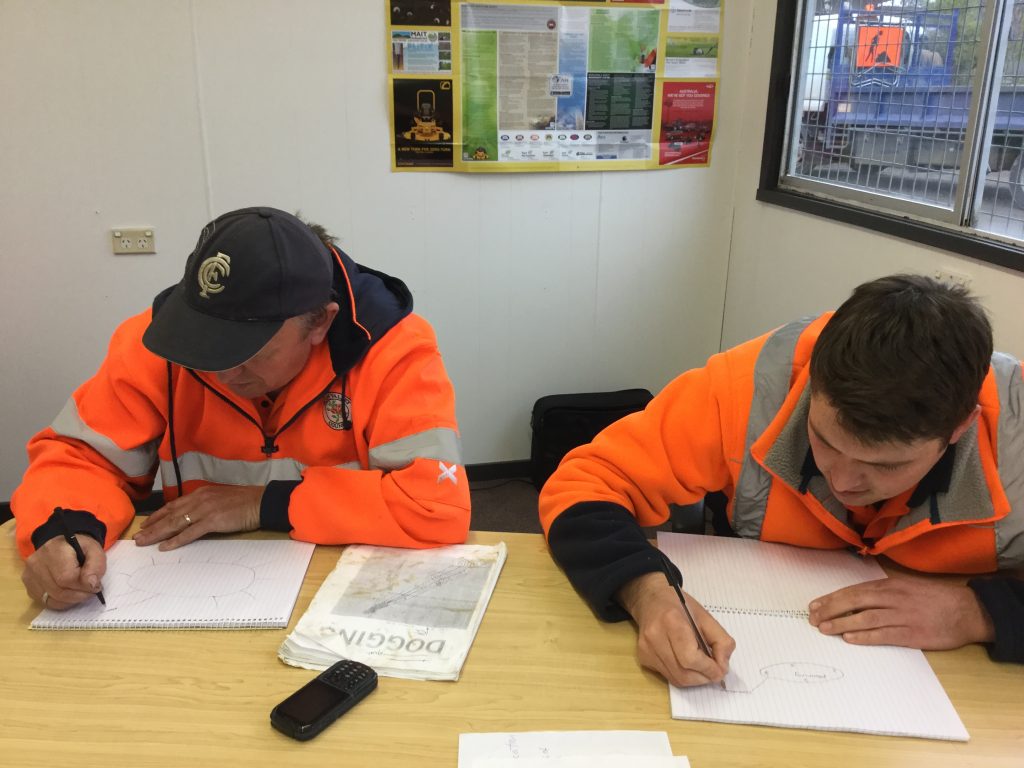 26Ten workplace grant project - Huon Valley Council. Two people in high visibility clothing, sitting a table and writing.